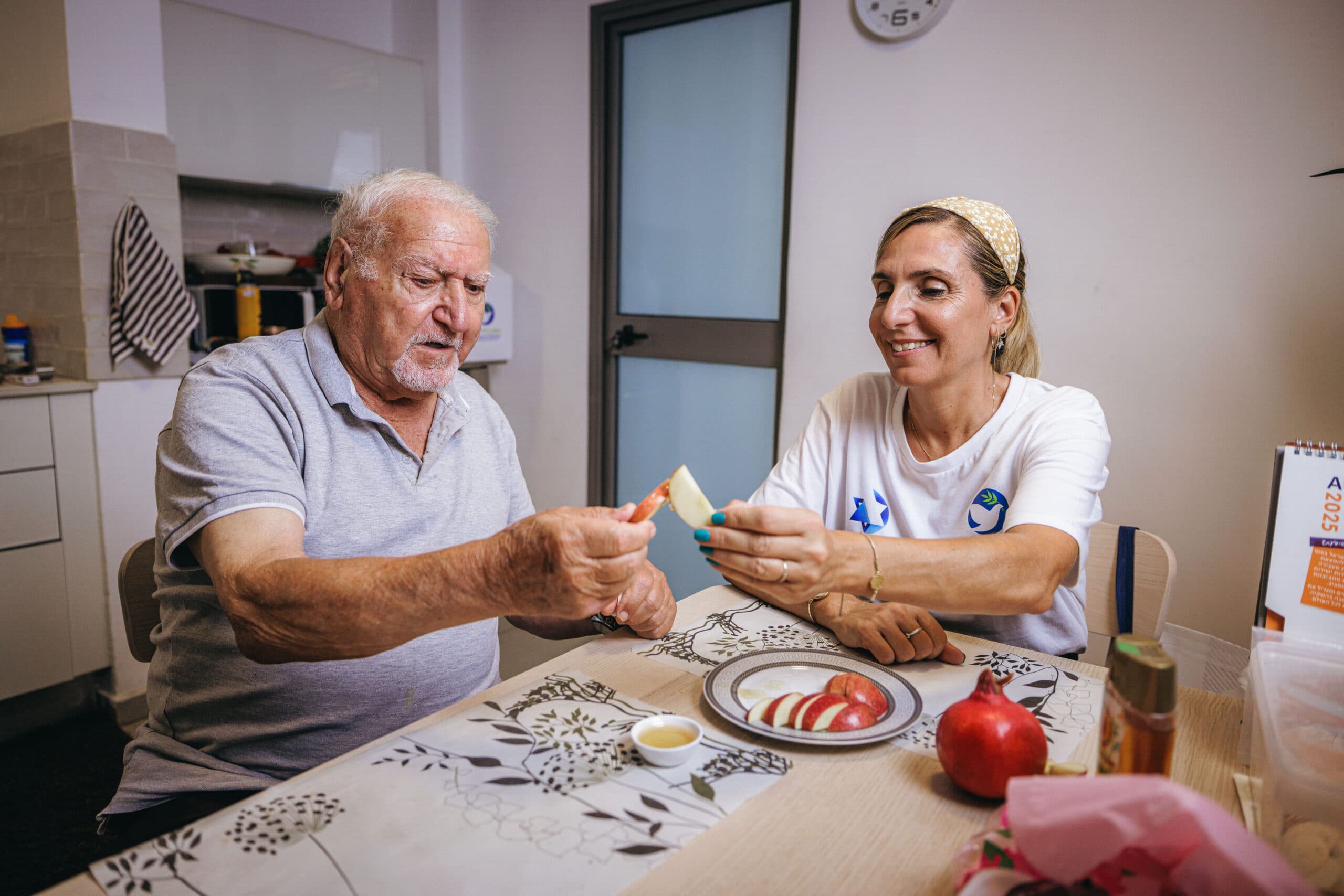 מתנדבת של הקרן לידידות חוגגת עם קשיש את ראש השנה בשולחן עם תפוח ודבש.
